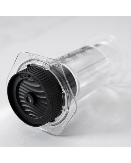 Tapa Flow Control enroscada en una AeroPress Clear apoyada sobre encimera de mármol