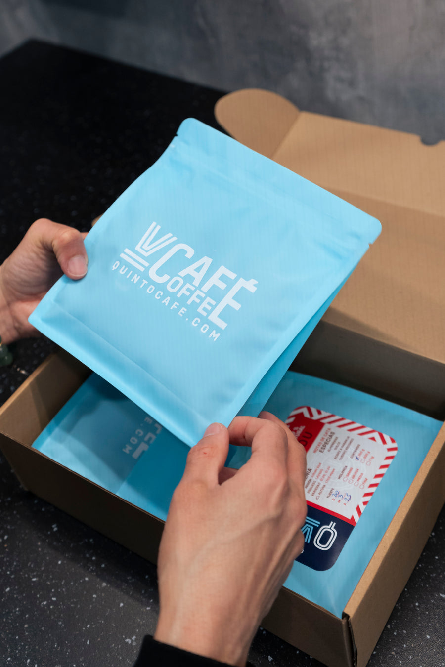 Manos abriendo la caja de envío de Quinto Café con la bolsa de café