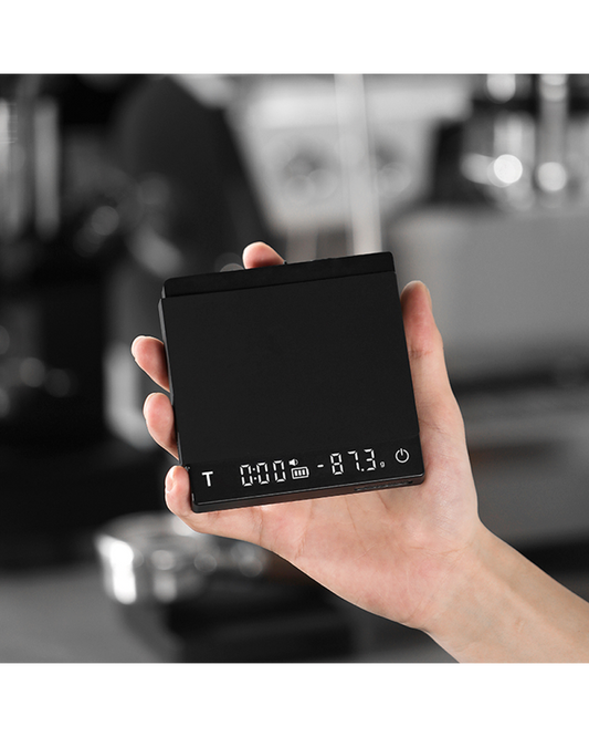 Mano sujetando la báscula Cube 2.0 Mini encendida con temporizador y peso en pantalla